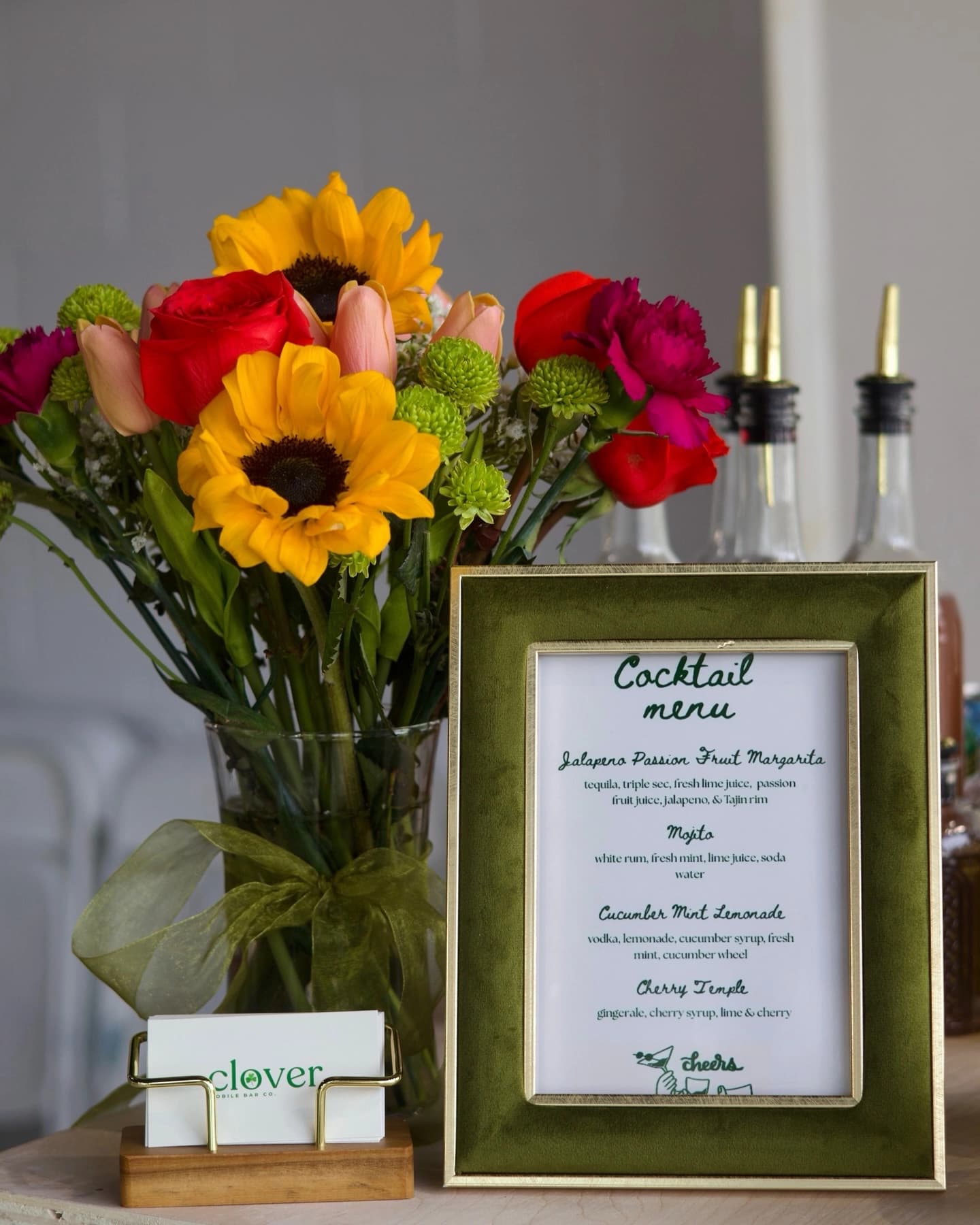 A printed cocktail menu in a green velvet frame on the Clover bar.